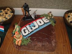 there is a cake with the word g i joe on it and some cookies in bowls