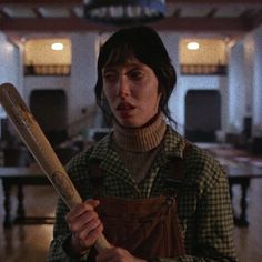 a woman holding a wooden baseball bat in a room filled with tables and chairs,