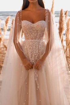 a woman in a wedding dress standing on the beach with her arms behind her back