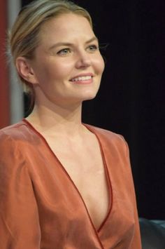 a woman in an orange dress smiles at the camera while sitting on a black chair