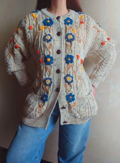 a woman is standing in front of a wall wearing a sweater with flowers on it