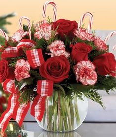 a vase filled with red roses and candy canes on top of a table next to a christmas tree