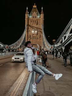 a woman leaning on a fence in front of a bridge at night with cars and pedestrians