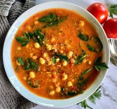 a white bowl filled with soup and garnished with fresh basil, tomatoes and chickpeas