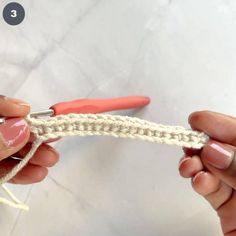 two hands crocheting the end of a piece of white yarn with red scissors