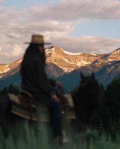 two people riding horses in front of mountains