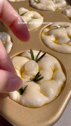 a person placing some food in a muffin tin with rosemary sprigs on top