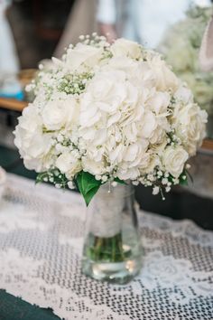 a vase filled with white flowers sitting on top of a lace covered table cloth next to a mirror