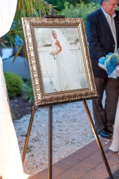 an easel with a picture frame on it next to a bride and groom in the background