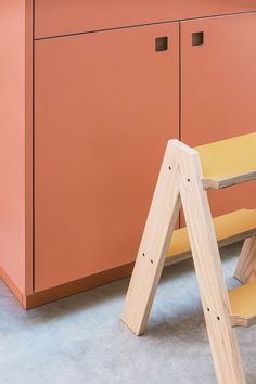 a wooden bench sitting in front of a pink cabinet next to a pair of ladders