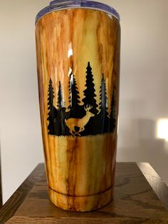 a wooden cup with an image of a deer and trees on it sitting on a table