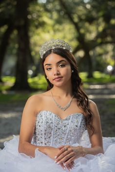 a woman wearing a tiara sitting on the ground in front of trees and grass