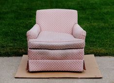 a pink chair sitting on top of a cardboard box in front of some green grass