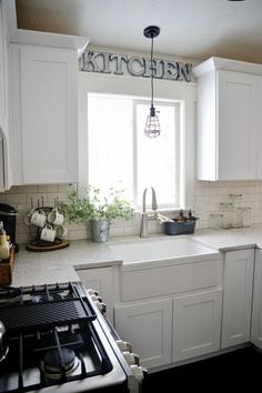 a kitchen with white cabinets and black stove top burner, window over the sink