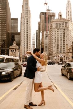 a man and woman kissing on the street in front of tall buildings with cars passing by