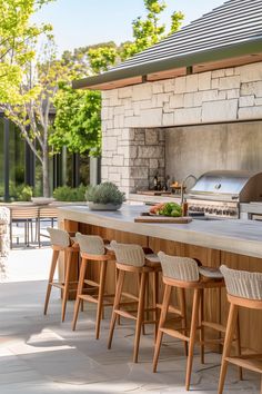 an outdoor kitchen with bar stools next to it and grill in the back ground