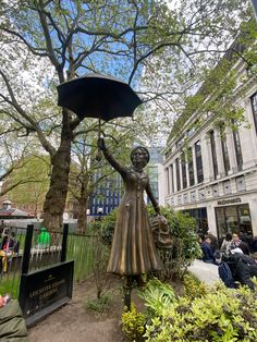 a statue of a woman holding an umbrella in the middle of a park with people sitting on benches