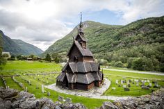 an old wooden church in the middle of a cemetery with mountains in the back ground