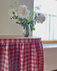 a vase filled with white flowers sitting on top of a red and white checkered table cloth