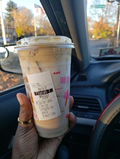 a person holding up a cup of coffee in their hand while sitting in the backseat of a car