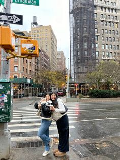 two women standing on the side of a road in front of tall buildings and traffic lights