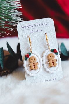 the gingerbread man earrings are on display next to a christmas tree and pine cones