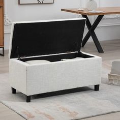 a white storage ottoman with black top and legs in a living room next to a coffee table