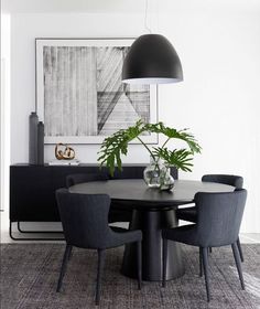 a dining room table with chairs and a potted plant in the center, next to an art piece