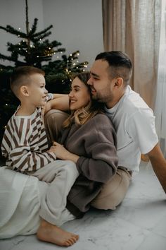 a man, woman and child sitting on the floor in front of a christmas tree