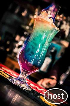 a colorful drink sitting on top of a table next to a person at a bar