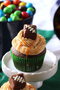 two cupcakes with football decorations on them are sitting on a plate next to some candy