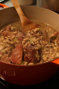 beans, ham and broccoli are being cooked in a pot with a wooden spoon