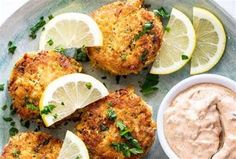 crab cakes with tartar sauce and lemon wedges on a blue plate next to a small bowl of dipping sauce