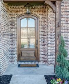 the front door to a brick house with an arched wooden frame and glass pane