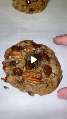 two chocolate chip cookies with pecans and nuts on top, being held by someone's hand