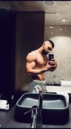 a shirtless man taking a selfie in front of a bathroom mirror with his cell phone