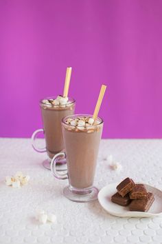 two glasses filled with hot chocolate and marshmallows on a white tablecloth