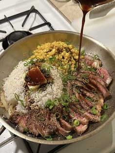 a pan filled with meat, rice and corn on top of a stove burner