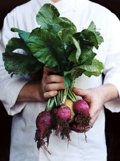 a man holding up some radishes and green leafy greens in his hands