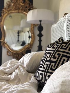 a bed with white sheets and pillows in front of a large mirror on the wall