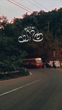 a bus driving down a road next to a lush green forest under a cloudy sky