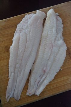 two pieces of raw fish sitting on top of a wooden cutting board