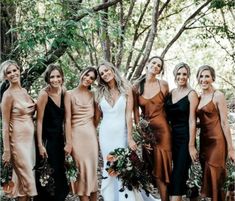 a group of women standing next to each other in front of trees and bushes with one woman wearing a brown dress