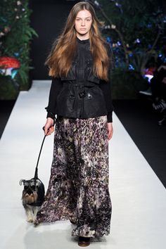 a woman is walking her dog down the catwalk wearing a black jacket and floral pants