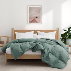 a bed with green comforter and pillows in a white room next to a potted plant