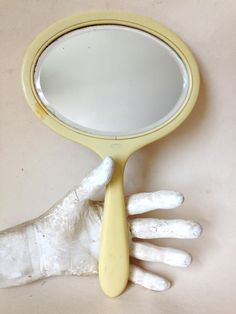 a hand holding a yellow mirror with white paint on it's fingers and palm