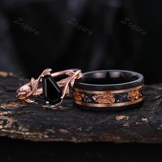 two wedding bands with black diamonds and gold leaf designs on them sitting on a piece of wood