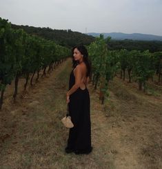 a woman in a long black dress is walking through the vineyard