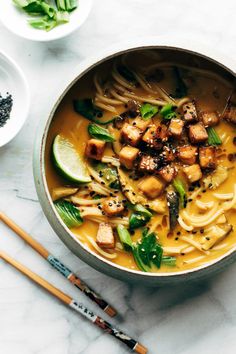 a bowl filled with noodles and tofu on top of a table next to chopsticks