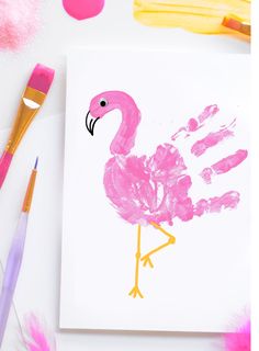 a pink flamingo handprint on a white paper with paintbrushes next to it